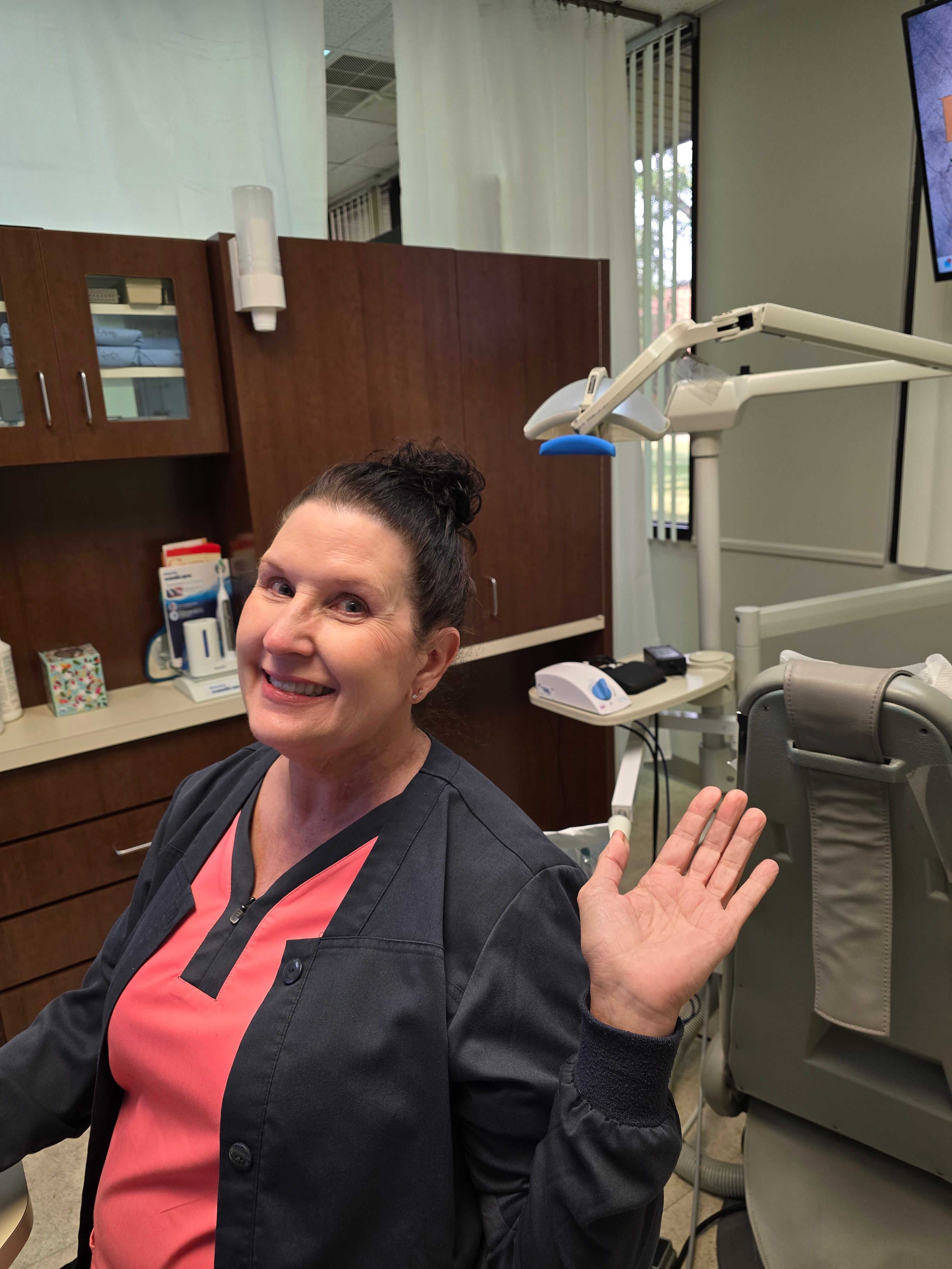 a woman is sitting in a dental chair waving at the camera .