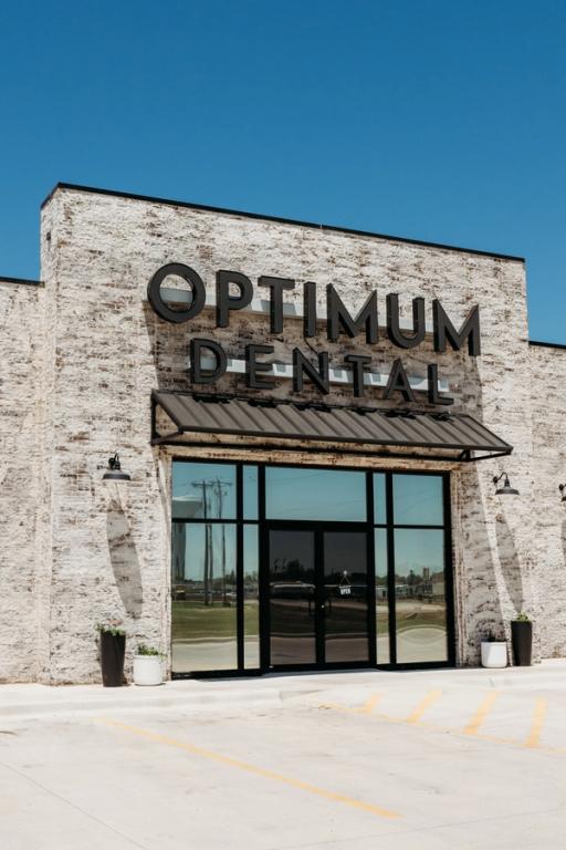 Optimum Dental building exterior with light brick and large glass entrance.
