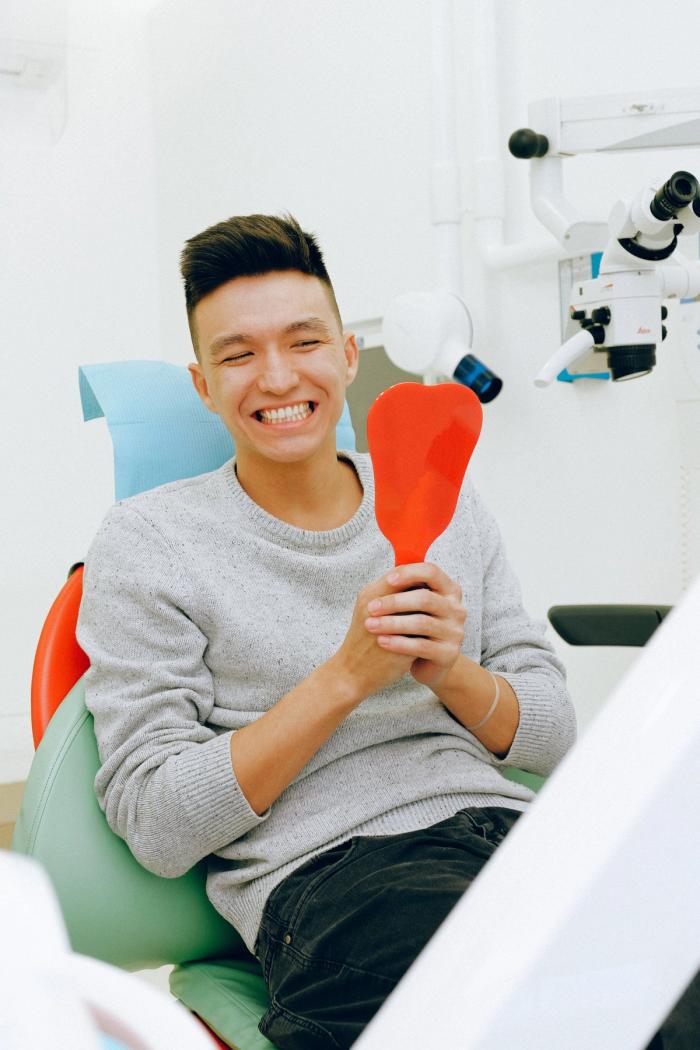 a man sitting in a dental chair looking at his teeth in a mirror