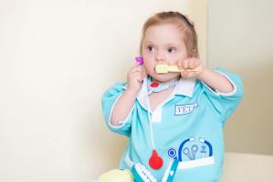 A young girl wearing a "VET" scrub top and toy stethoscope holds toy medical instruments.