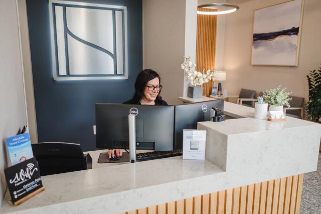 a woman is sitting at a desk in front of a computer in a dental office .