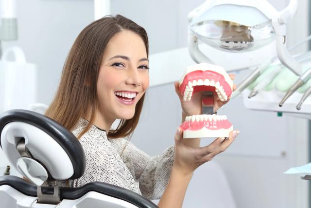 a woman is sitting in a dental chair holding a model of her teeth .