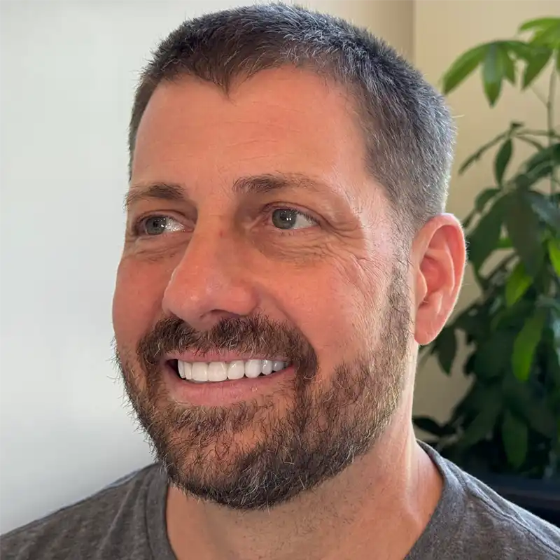 a man with a beard is smiling with a plant in the background