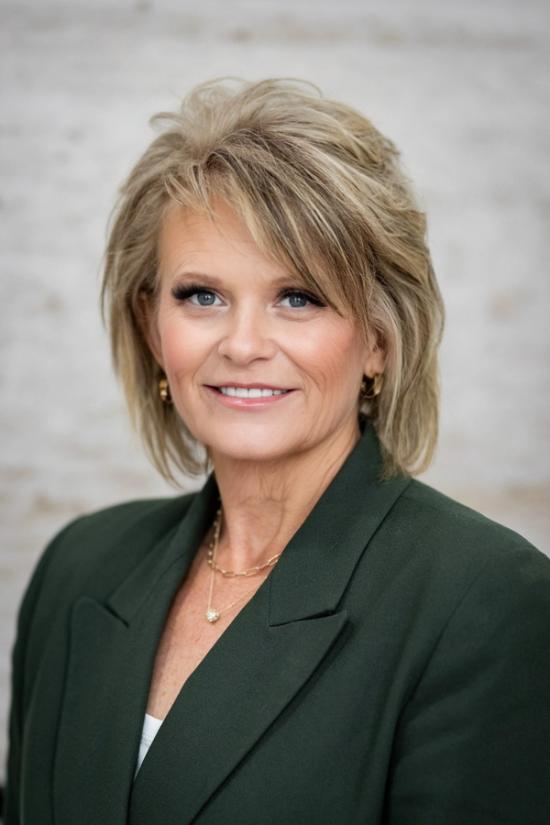 a woman wearing a green jacket and a gold necklace is smiling for the camera .