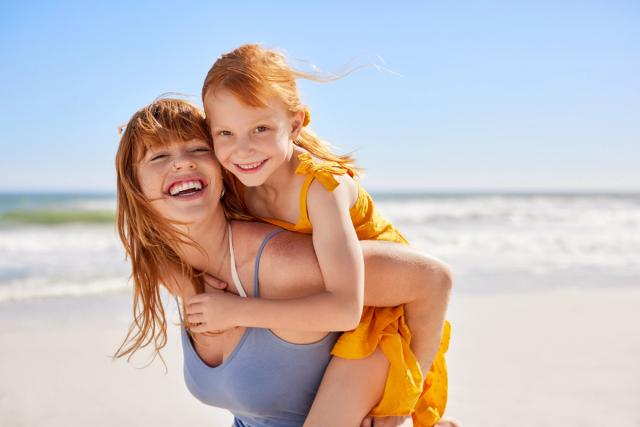 a woman is giving a little girl a piggyback ride on the beach .