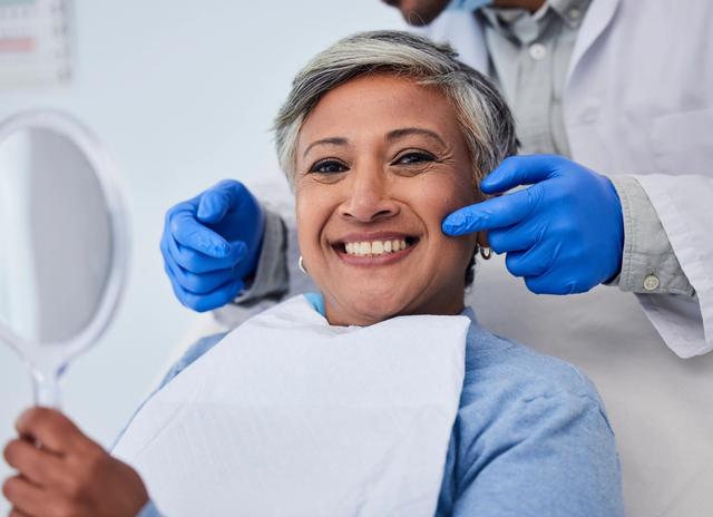 a woman is smiling while looking at her teeth in a mirror .