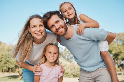 a family is posing for a picture while a man is carrying two girls on his back .