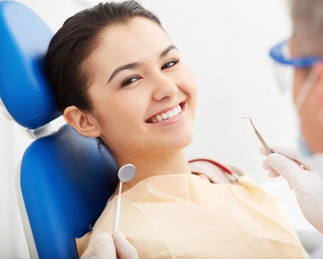 a woman is sitting in a dental chair while a dentist examines her teeth .