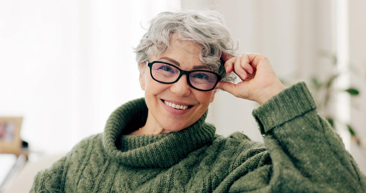 an older woman wearing glasses and a green sweater is smiling .