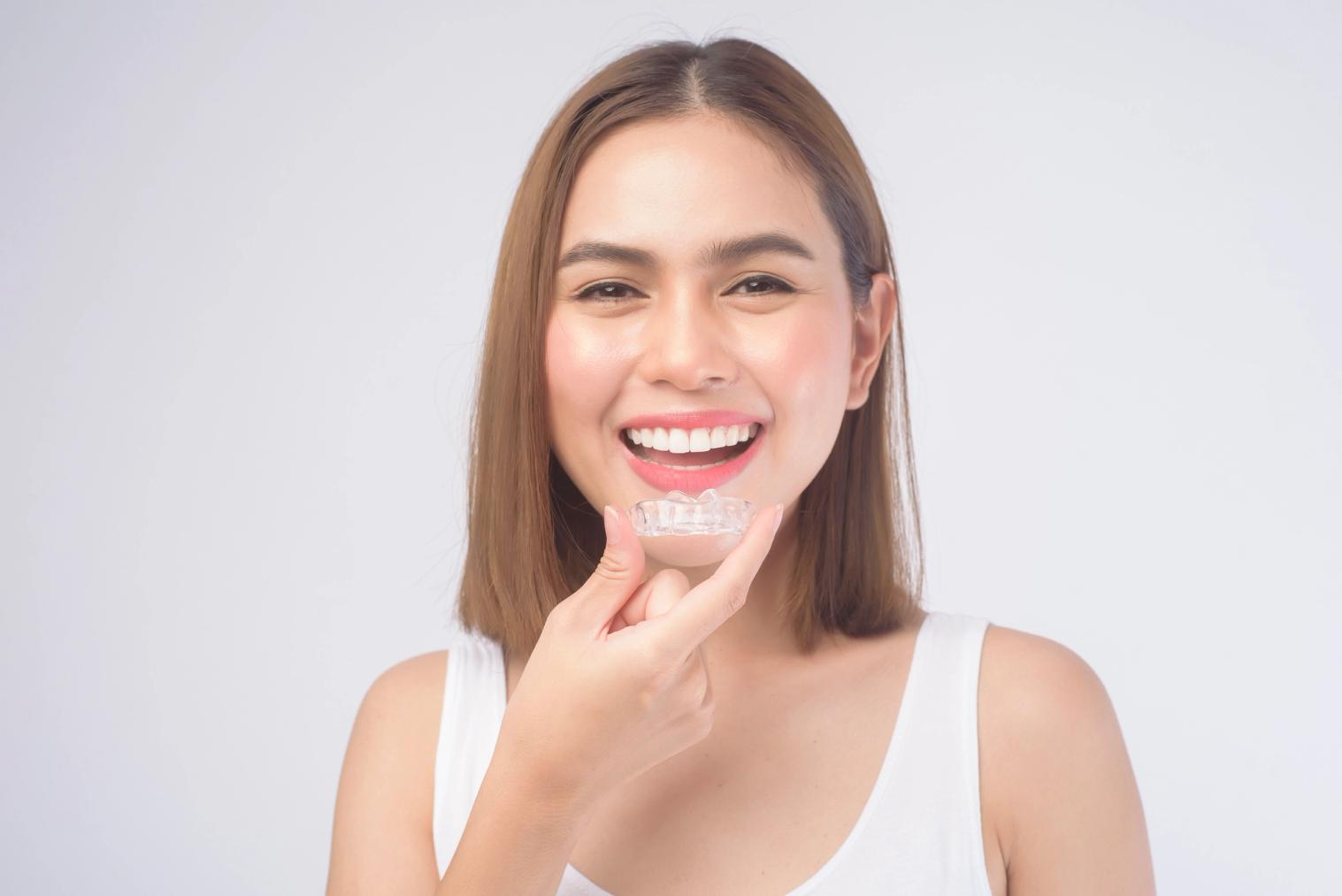 Smiling woman holding a clear dental aligner.