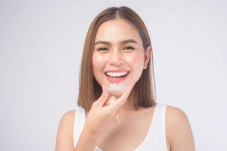 a woman is smiling while holding a clear brace on her teeth .