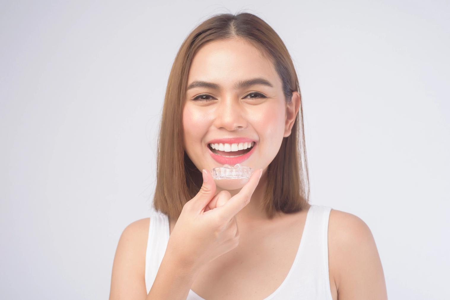 Smiling woman holding a clear dental aligner.