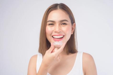 a woman is smiling while holding a clear brace on her teeth .