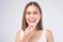 A smiling woman holds a clear dental aligner to her mouth.