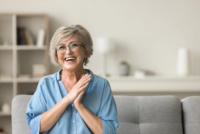 an elderly woman is sitting on a couch with her hands on her chest and smiling .