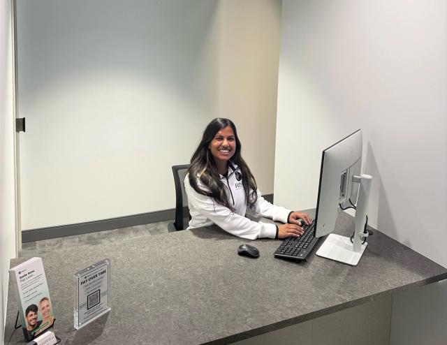 A smiling woman in a white "Smile Space" jacket sits at a reception desk, typing on a computer.