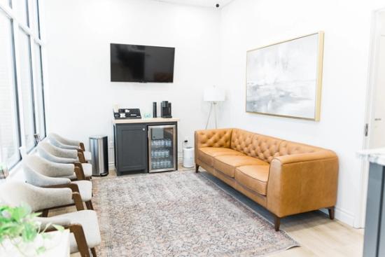 a waiting room with a couch , chairs , a television and a refrigerator .