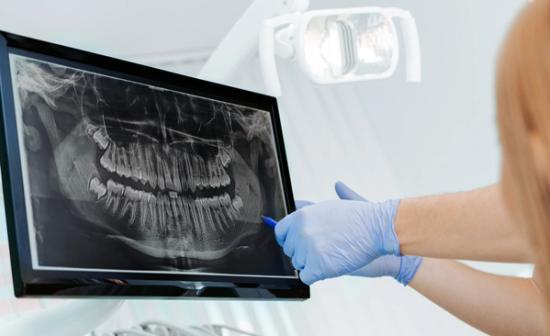 a dentist is looking at an x-ray of a person 's teeth on a computer screen .