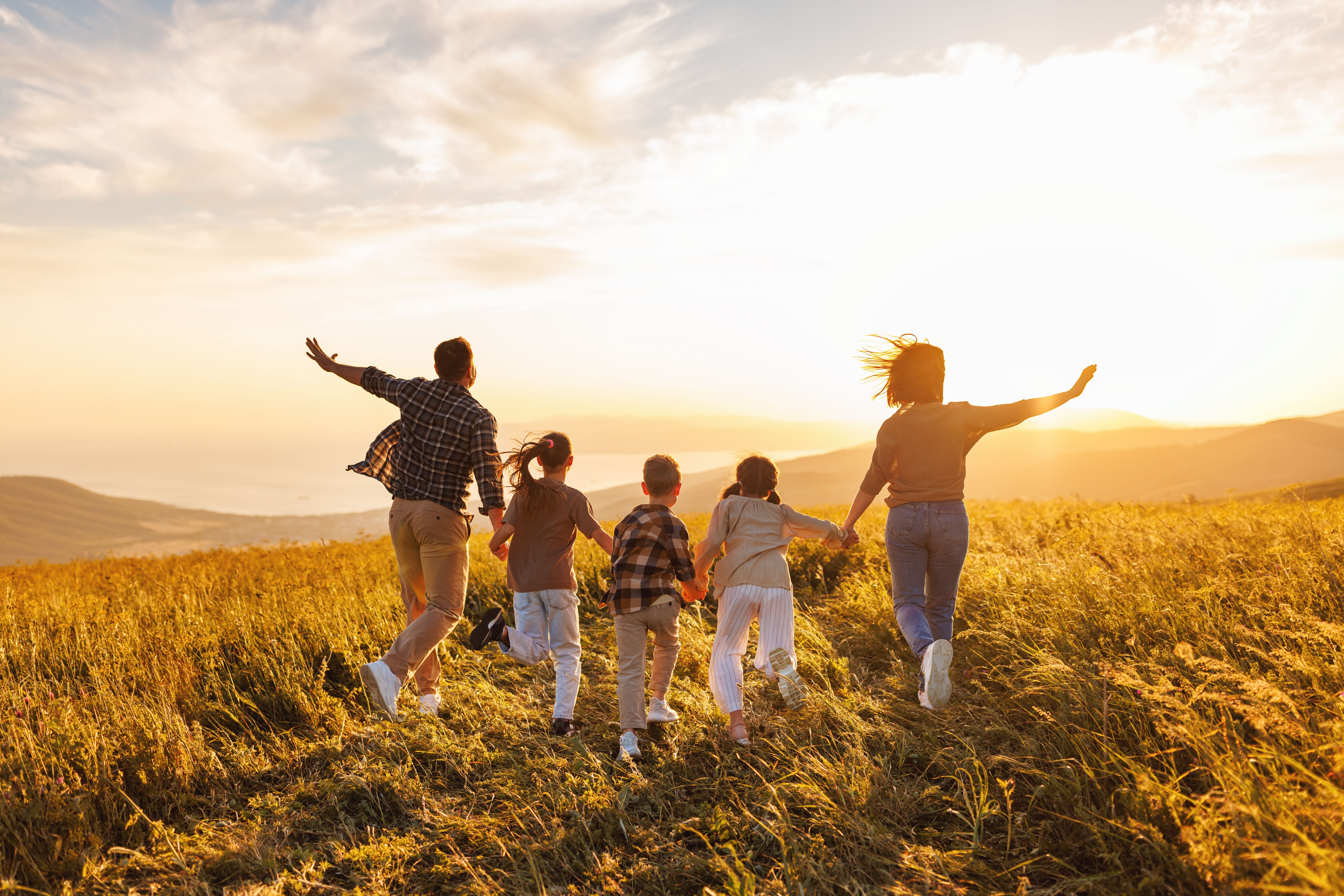 a family is running through a field at sunset .
