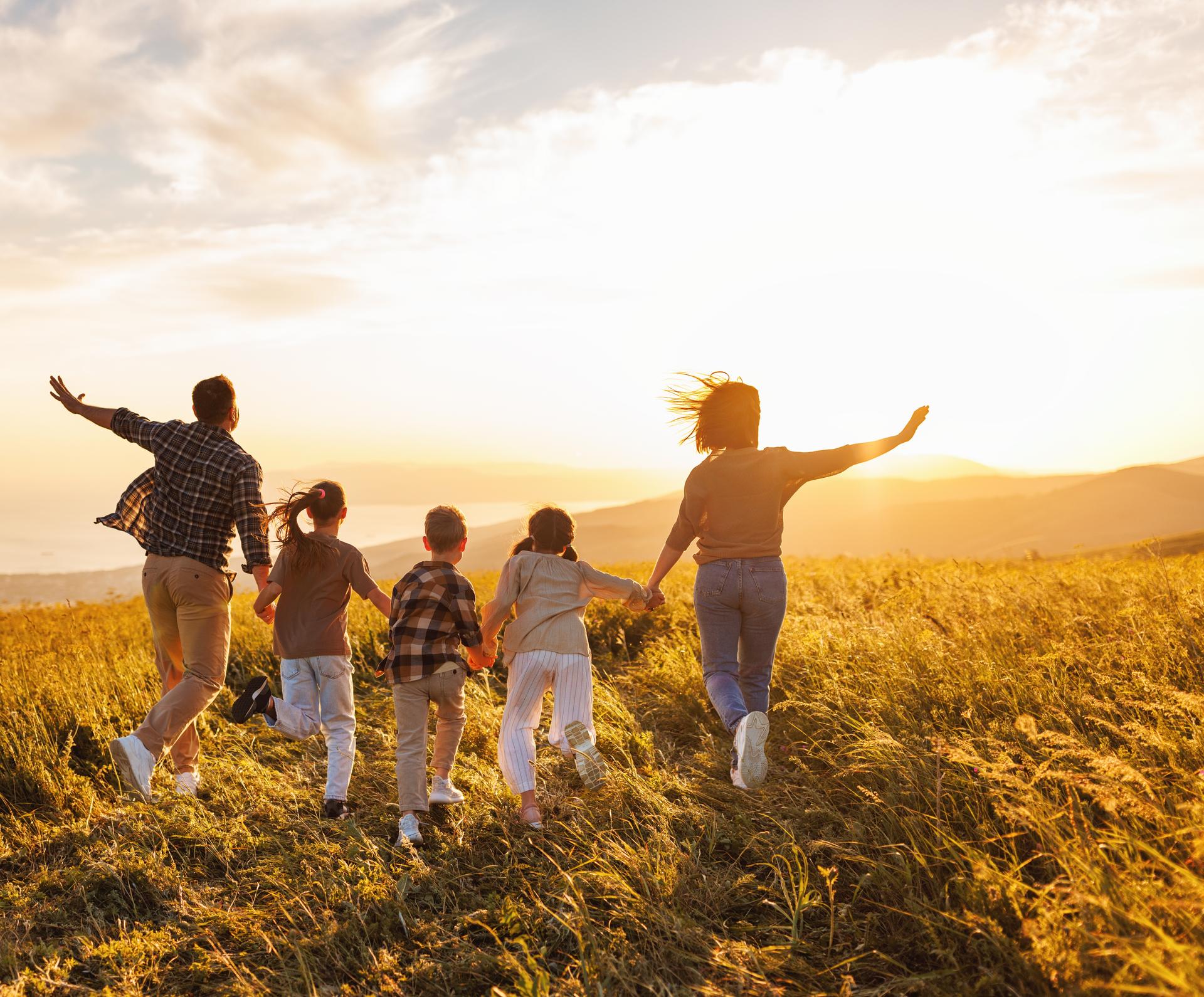 a family is running through a field at sunset .