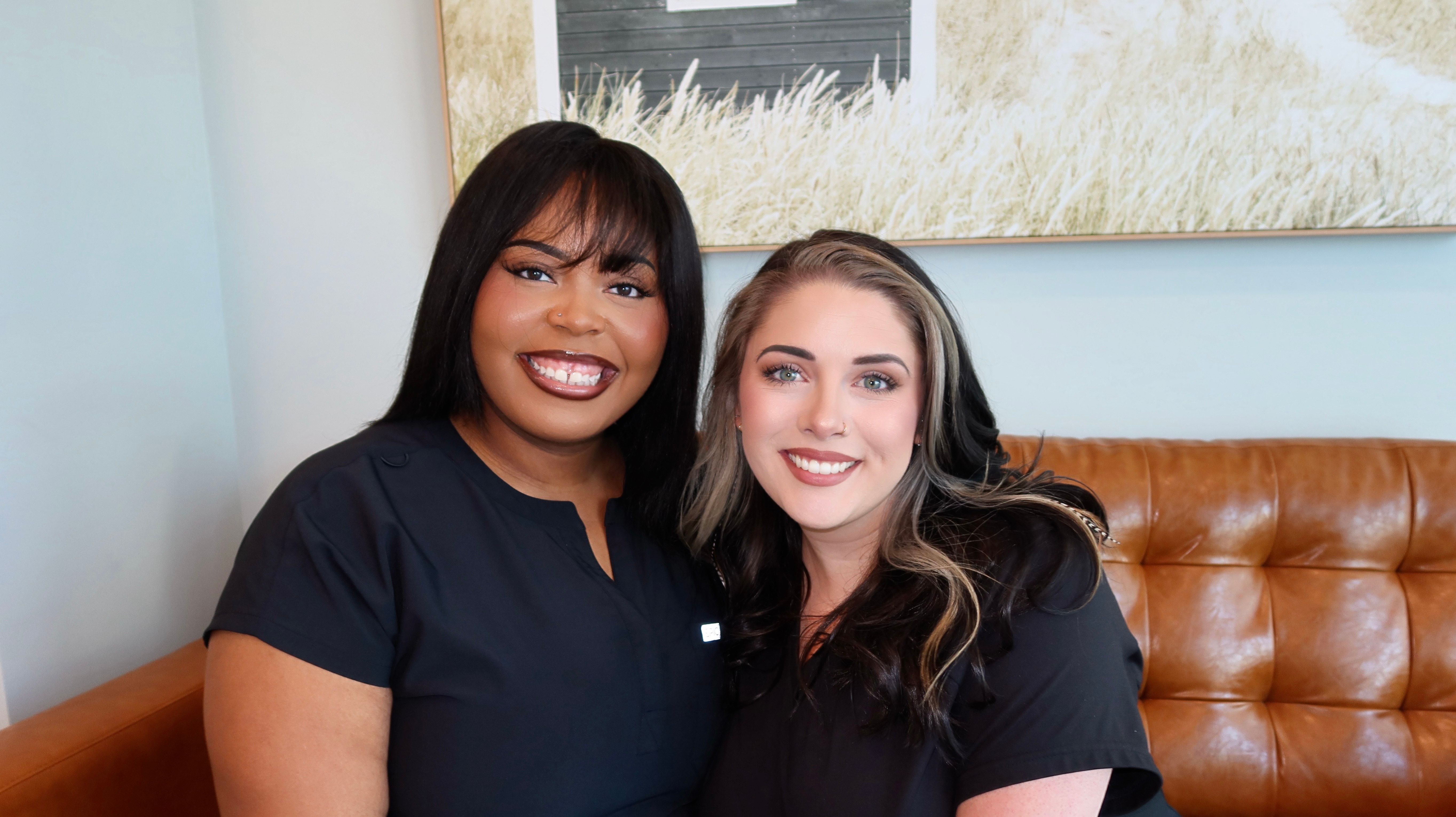 two women are sitting next to each other on a couch and smiling for the camera .