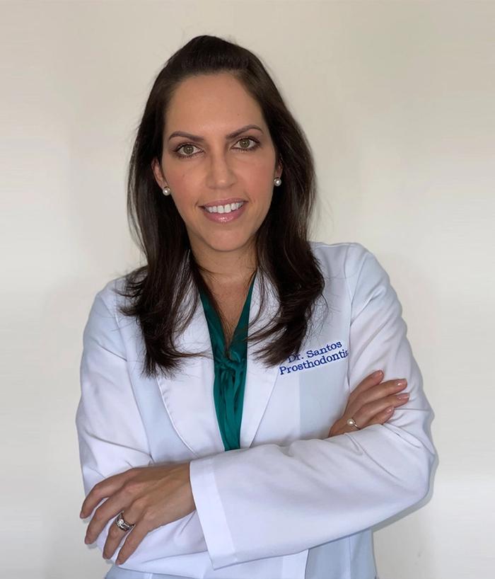 a woman in a white lab coat is standing with her arms crossed and smiling .
