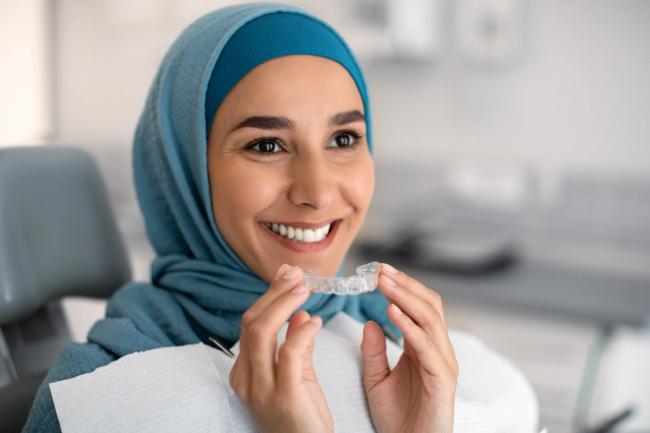 a woman in a hijab is smiling while holding a clear braces .