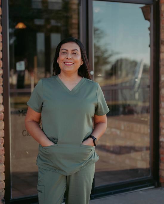 Smiling woman in green scrubs with hands in pockets.