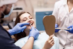 a woman is sitting in a dental chair looking at her teeth in a mirror .