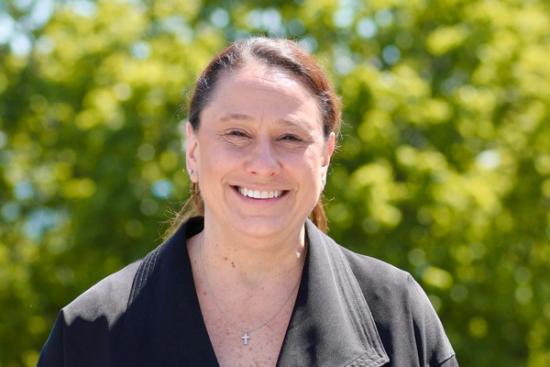 a woman wearing a black jacket and a cross necklace is smiling for the camera .
