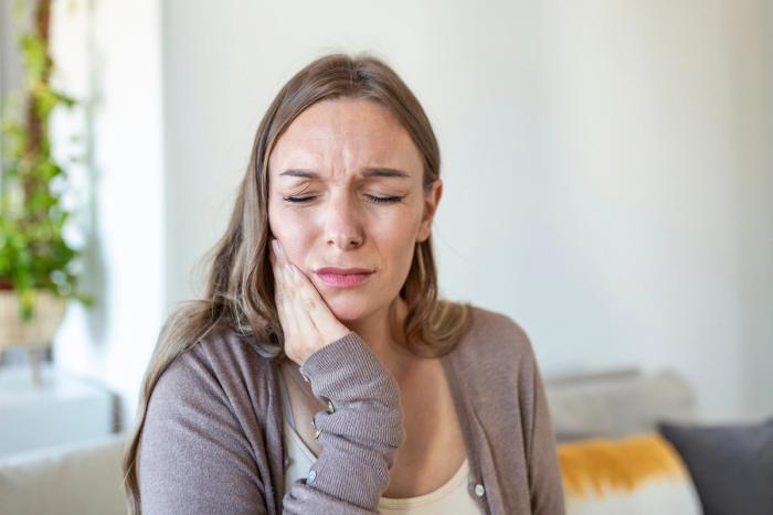 a woman is holding her mouth in pain while sitting on a couch .