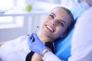 Smiling woman in a dental chair with a dentist's gloved hand holding a dental mirror.