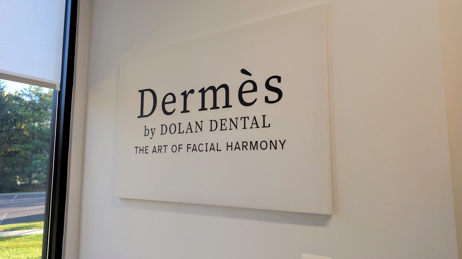 A white sign on a wall displays "Dermès by DOLAN DENTAL THE ART OF FACIAL HARMONY".