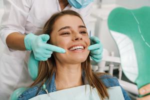 Smiling woman in a dental chair looking at her bright teeth in a mirror, assisted by a dentist.