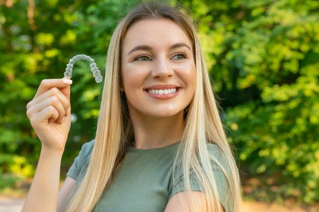 Smiling woman holding a clear dental aligner.