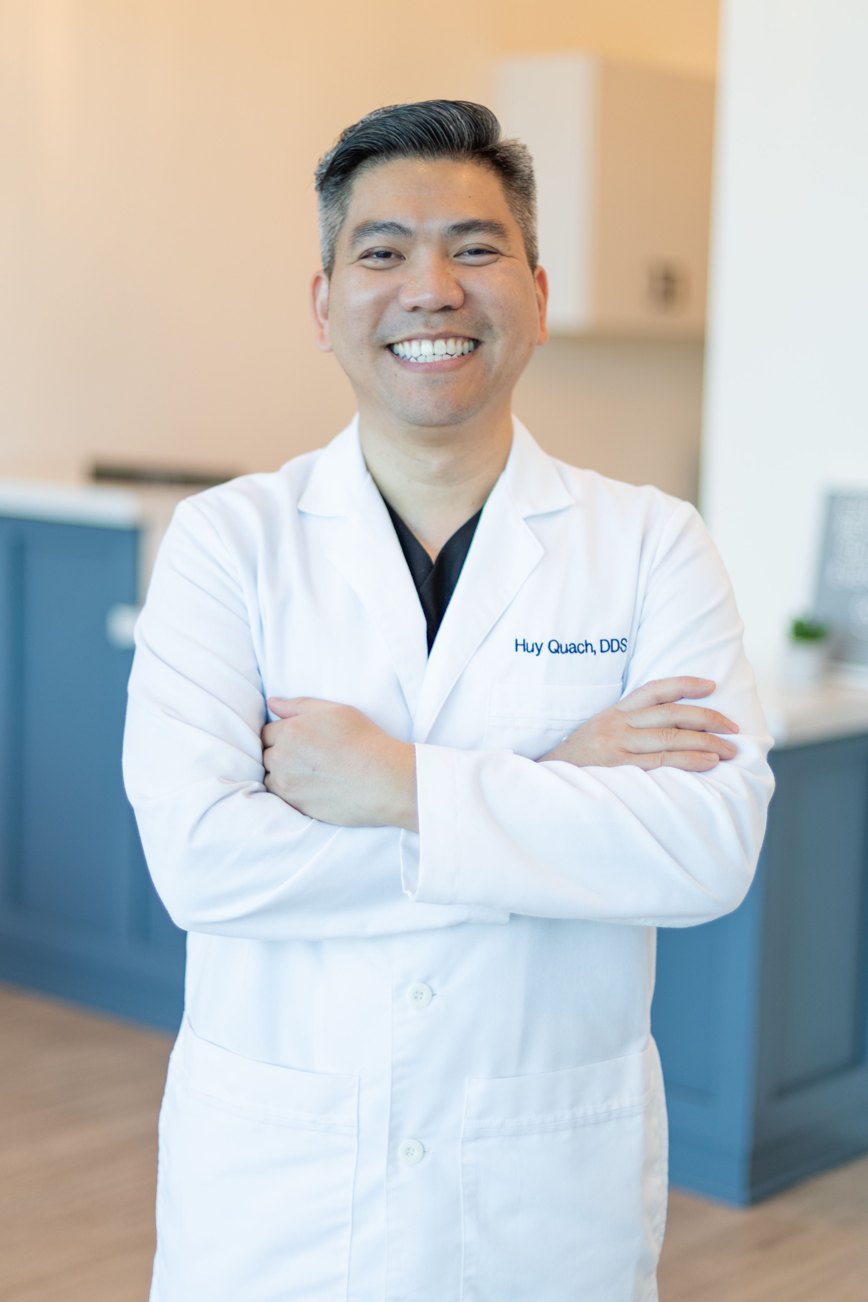 a man in a white lab coat is smiling with his arms crossed .