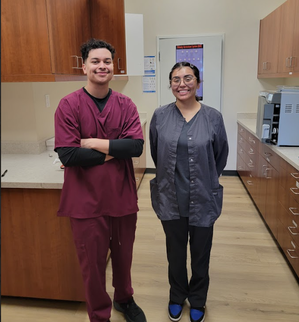 A smiling man and woman in scrubs stand in a medical office.