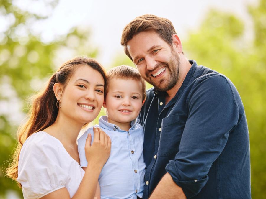 A smiling family of three: a woman, man, and young boy, posing outdoors.