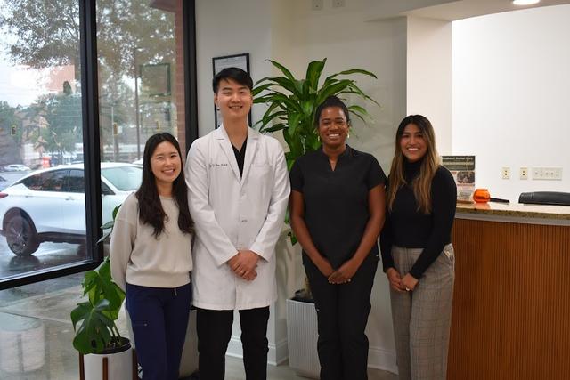 A team of four, including a doctor in a white coat, smiles in an office reception area.