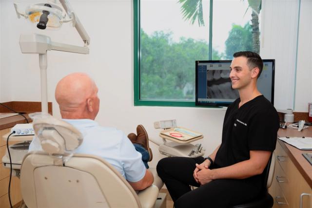 a man is sitting in a dental chair talking to a dentist .