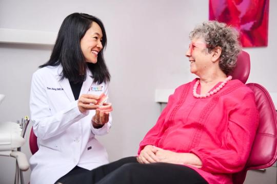 a dentist is talking to an older woman in a pink shirt in a dental chair .