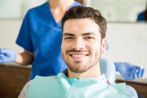 Smiling man in a dental chair with a bib, a dental professional behind him.