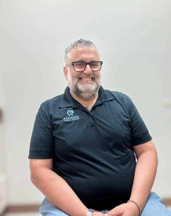 a man with a beard and glasses is wearing a black polo shirt .