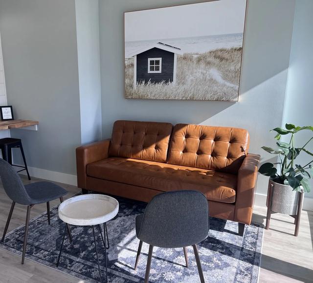 a living room with a brown couch , chairs , a table and a painting on the wall .