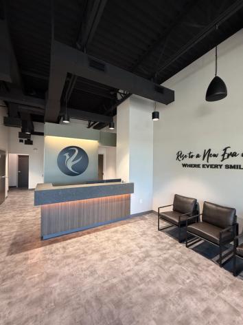 Modern reception area with a lit reception desk, a logo wall, dark waiting chairs, and a slogan "Rise to a New Era" under an industrial black ceiling.