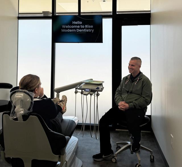 A patient in a modern dental chair faces a screen displaying "Welcome to Rise Modern Dentistry" while a smiling dentist sits nearby.