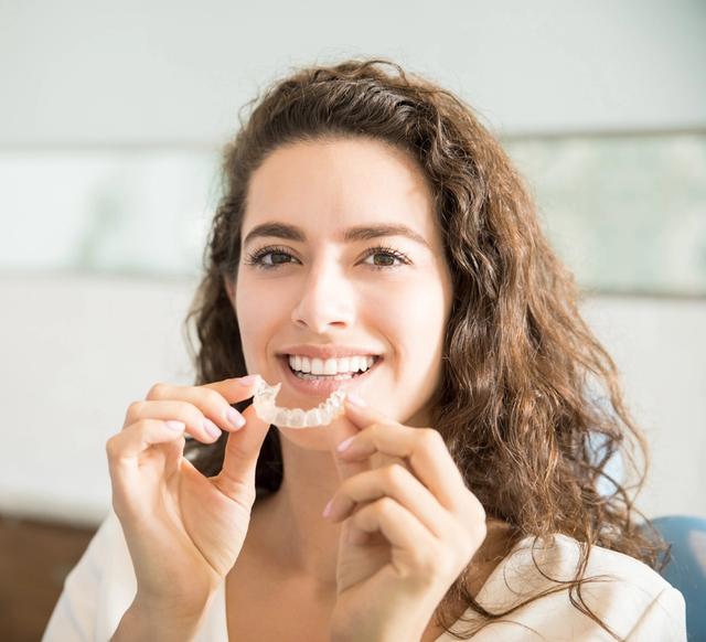 a woman is holding a clear braces in her hands and smiling .