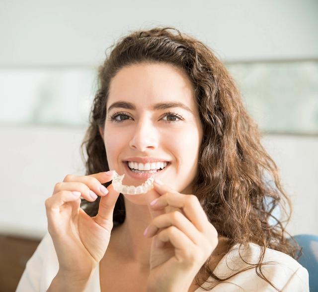 a woman is holding a clear braces in her hands and smiling .