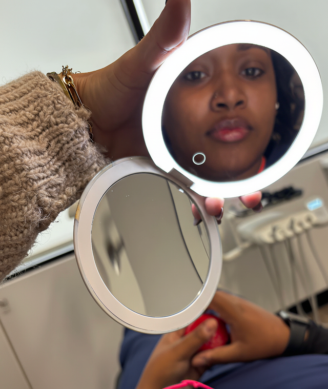 An illuminated compact mirror held by a hand reflects a woman's face.