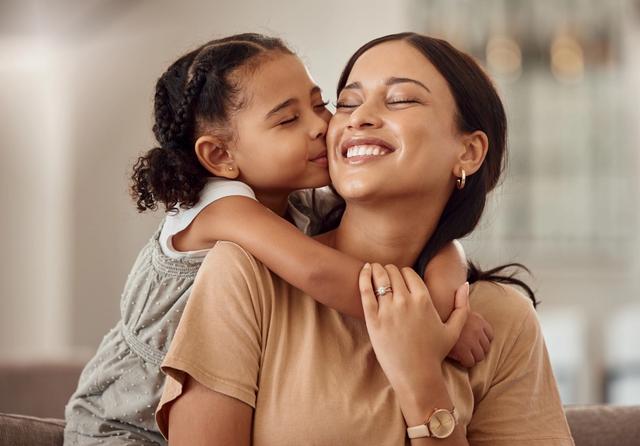 a little girl is kissing her mother on the cheek while sitting on a couch .